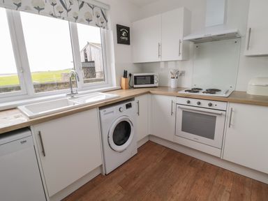 A kitchen with white cabinets wooden countertops a washing machine an oven a microwave and a window with a view at Seaview Howick in Craster