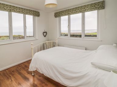 A bedroom with a white bed and large windows showing a sea view at Seaview Howick in Craster