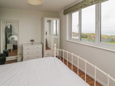 A bedroom with a bed a chest of drawers a wardrobe a wall mirror and a window overlooking a garden and stone wall at Seaview Howick in Craster