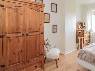A bedroom with a wooden wardrobe a white chair with a cushion a wooden chest of drawers and a bed at Seaview Howick in Craster