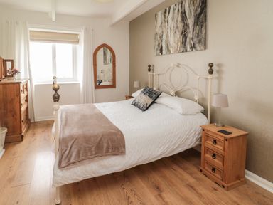 A bedroom with a cream metal bed frame wooden bedside tables a wooden dresser a wall mirror and a window at Seaview Howick in Craster