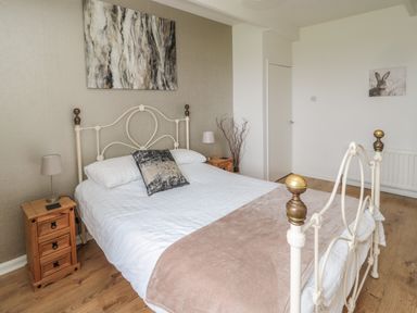 A bedroom with a metal bed frame a painting above the bed and bedside tables with lamps at Seaview Howick in Craster