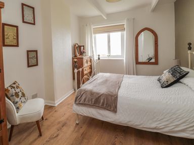 A bedroom with a bed white curtains a wooden dresser a wall mirror and a chair with a cushion at Seaview Howick Craster