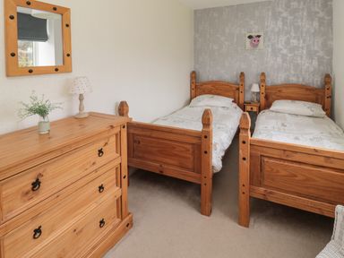 A bedroom with two wooden single beds a wooden chest of drawers a small bedside table with a lamp and a mirror on the wall at Seaview Howick Craster