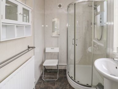 A bathroom with a corner shower cubicle a white sink a small mirror a white chair a wall cabinet and a radiator at Seaview Howick in Craster