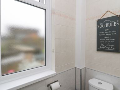 A bathroom with a frosted window a toilet paper holder a toilet and a hanging sign with bathroom rules at Seaview Howick in Craster