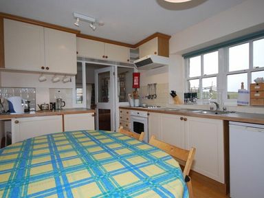 A kitchen with white cabinets, a round table with a yellow and blue checkered tablecloth, and a window at Snook Point Cottage in Newton-by-the-Sea
