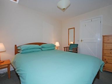 A bedroom with a double bed with teal bedding a wooden chair with teal cushion a wooden chest of drawers and two bedside lamps at Snook Point Cottage in Newton-by-the-Sea