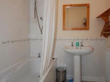 A bathroom with a bathtub and shower curtain a pedestal sink with a mirror above and a small trash can at Snook Point Cottage in Newton-by-the-Sea