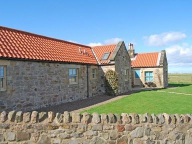 A stone cottage with a red tiled roof and a green lawn behind a stone wall at Snook Point Cottage in Newton-by-the-Sea