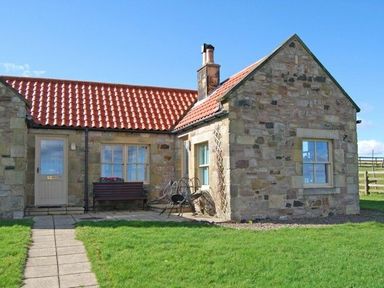 A stone cottage with red tile roof a door bench and lawn at Snook Point Cottage in Newton-by-the-Sea