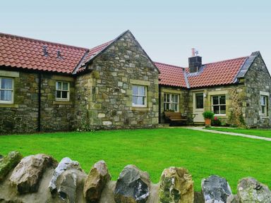 A stone cottage with a tiled roof and green lawn behind a stone fence at Snook Point Cottage in Newton-by-the-Sea