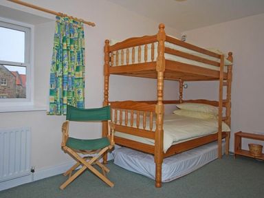 A bedroom with wooden bunk beds green folding chair window with patterned curtains and a small wooden table at Snook Point Cottage in Newton-by-the-Sea