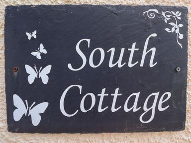 A sign with white butterflies and text South Cottage on a black background at South Cottage Howick Craster