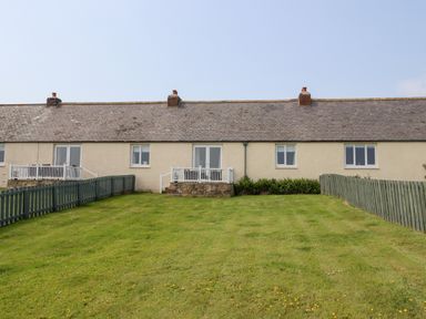 A row of single story houses with fenced yards and small patios at South Cottage Howick in Craster