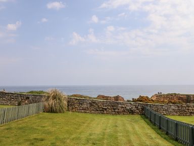 A grassy yard with stone and wooden fences overlooking the ocean at South Cottage Howick in Craster
