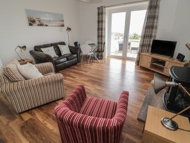 A living room with a striped armchair a leather sofa a striped sofa a glass dining table and chairs a television and patio doors at South Cottage Howick in Craster