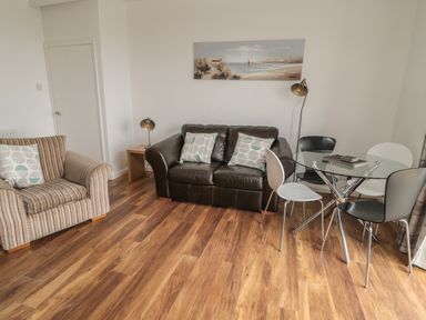 A living room with a striped armchair a black leather sofa with cushions a glass dining table with four chairs two lamps and a painting on the wall at South Cottage Howick in Craster