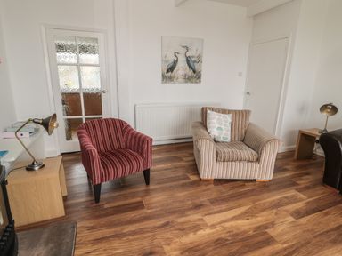 A room with two armchairs a wooden floor lamps a door and a painting of birds on the wall at South Cottage Howick in Craster
