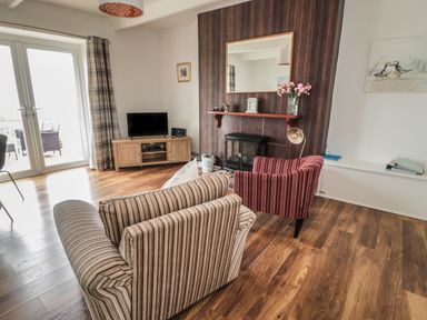 A living room with striped armchairs wooden floor a television a fireplace with a mirror and flowers at South Cottage Howick Craster