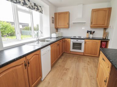 A kitchen with wooden cabinets black countertops a white oven dishwasher and a window overlooking a garden at South Cottage Howick in Craster