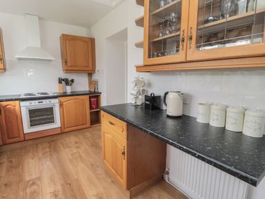 A kitchen with wooden cabinets and black countertops with electric stove kettle and storage jars at South Cottage Howick in Craster