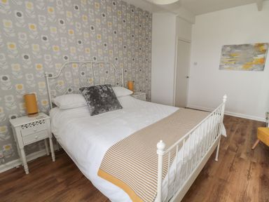 A bedroom with a white metal bed frame a patterned bed runner and floral wallpaper at South Cottage Howick Craster