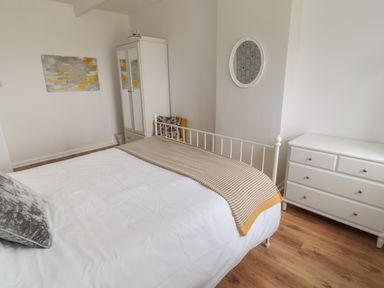 A bedroom with a white bed frame white dresser a white wardrobe wooden floor and wall art at South Cottage Howick in Craster