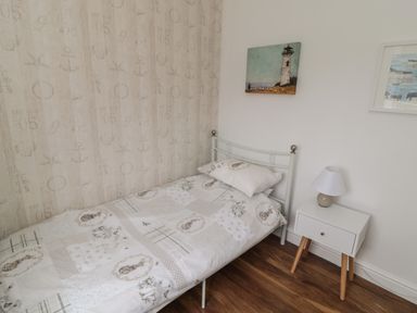 A bedroom with a single bed a bedside table with a lamp and two paintings on the wall at South Cottage Howick in Craster