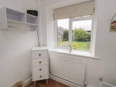 A corner of a room with a window looking out to a garden with green bushes a white four-drawer cabinet a wall-mounted shelf and a radiator below the window at South Cottage Howick in Craster