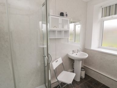 A bathroom with a shower enclosure sink mirror wall cabinet folding chair and frosted window at South Cottage Howick in Craster