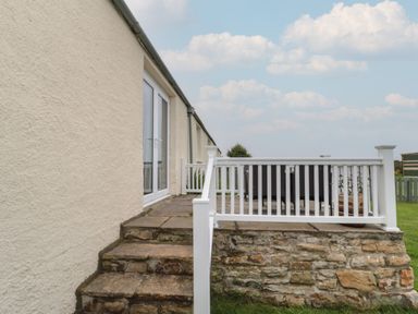 An outdoor patio with stone steps leading up to it and white railing around the patio at South Cottage Howick in Craster
