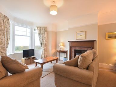 A living room with beige sofas wooden coffee table TV by window and fireplace with artwork at Ty y Mor in Seahouses