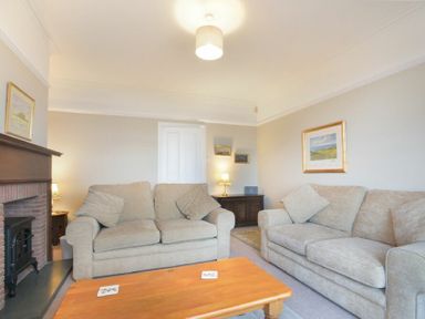 A living room with two beige sofas a wooden coffee table a fireplace and framed pictures on the wall at Ty y Mor in Seahouses