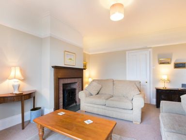 A living room with beige sofas a wooden coffee table lamps and a fireplace at Ty y Mor in Seahouses