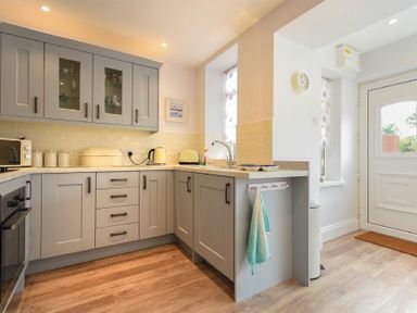 A kitchen with gray cabinets wooden flooring and a white door at Ty y Mor in Seahouses