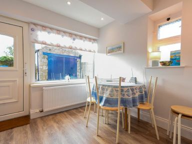 A dining area with a round table covered with a blue patterned tablecloth and four chairs near a window at Ty y Mor in Seahouses
