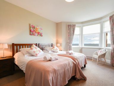 A bedroom with two single beds side by side with pink blankets and floral pillows at Ty y Mor in Seahouses