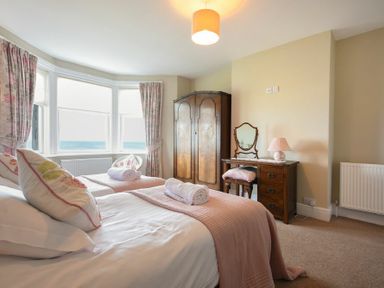 A bedroom with two beds a wooden wardrobe a dressing table and bay windows at Ty y Mor in Seahouses