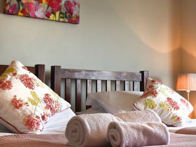 A bedroom with wooden headboard floral pillows rolled towels and a lamp at Ty y Mor in Seahouses