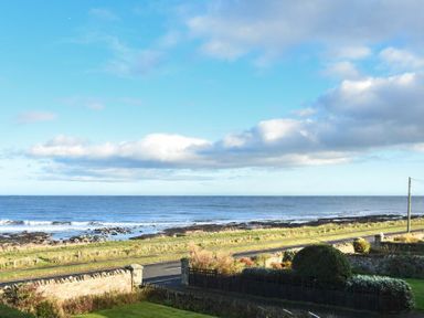 A coastal view with a road grassy area stone wall and ocean at Ty y Mor in Seahouses