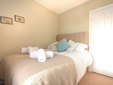 A bedroom with a bed with a beige headboard pillows and rolled white towels on the bed at Ty y Mor in Seahouses