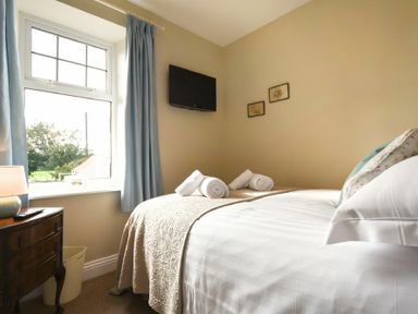 A bedroom with a bed with rolled towels a window with blue curtains a wooden bedside table and a wall-mounted tv at Ty y Mor in Seahouses