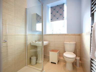 A bathroom with a shower enclosure a toilet a pedestal sink a small storage box and a window with patterned blind at Ty y Mor in Seahouses