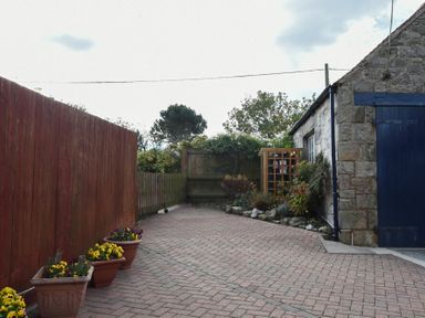 A paved driveway with potted plants along a wooden fence and a stone building with a blue door at Ty y Mor in Seahouses
