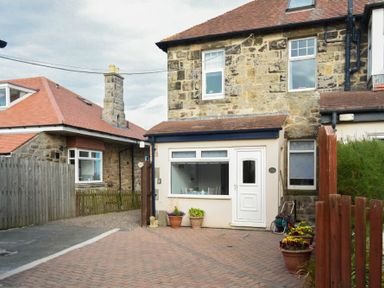 A stone house with a white door and window and flower pots outside at Ty y Mor in Seahouses
