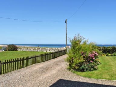 A gravel driveway with a wooden fence and green lawn with flowers by the seaside at Ty y Mor in Seahouses