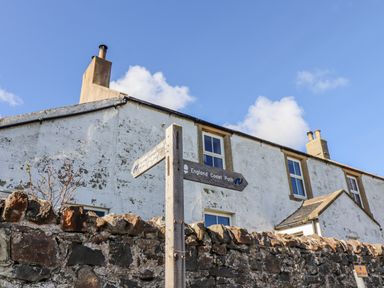 A house with a signpost indicating the England Coast Path at St Marys Cottages No4 Low Newton-by-the-Sea