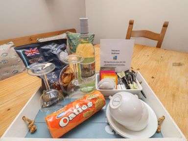 A wooden table with a tray holding a bottle of wine two wine glasses a packet of crisps a pack of oatcakes tea bags and cups at The Boathouse (Seahouses) in Seahouses