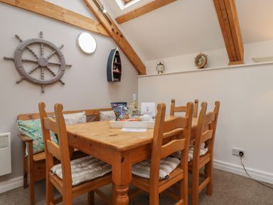 A dining area with a wooden table and six chairs with cushions under exposed wooden beams at The Boathouse (Seahouses) in Seahouses